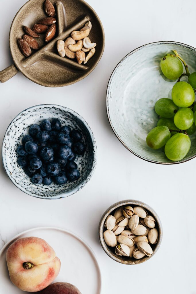 Healthy natural foods including fruits, nuts and seeds in ceramic bowls on a white background.